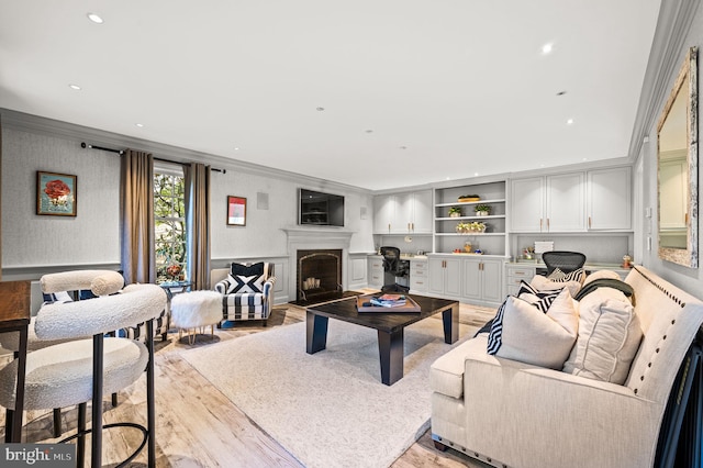 living area with crown molding, recessed lighting, a fireplace with raised hearth, and light wood-type flooring