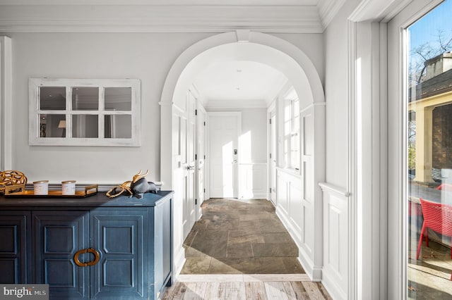 corridor with arched walkways, stone finish flooring, and ornamental molding