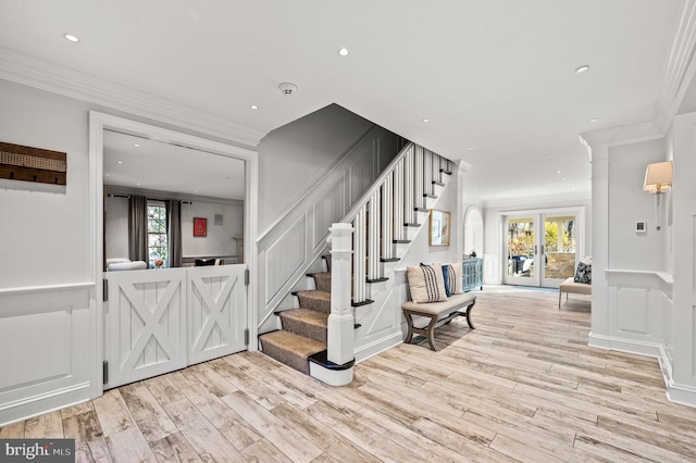 foyer featuring stairway, light wood-style flooring, crown molding, and a decorative wall