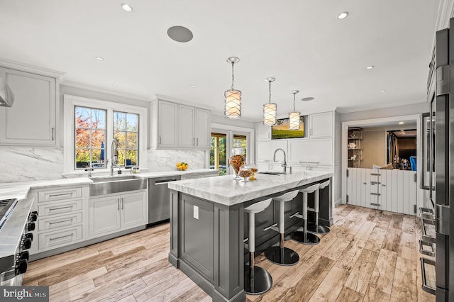 kitchen with tasteful backsplash, ornamental molding, light wood-style flooring, stainless steel appliances, and a sink