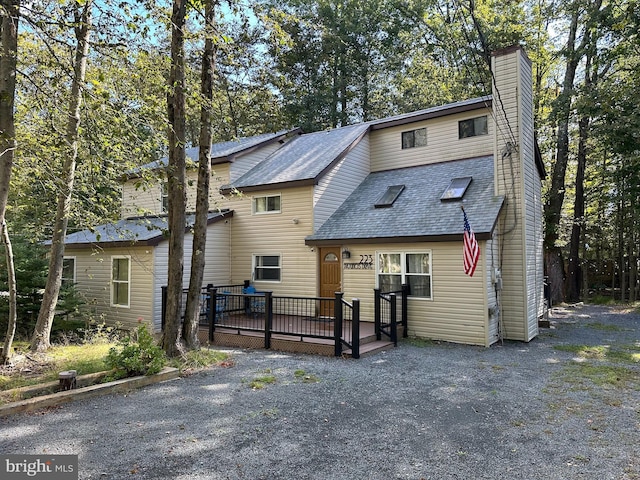 view of front facade featuring a wooden deck, roof with shingles, and a chimney