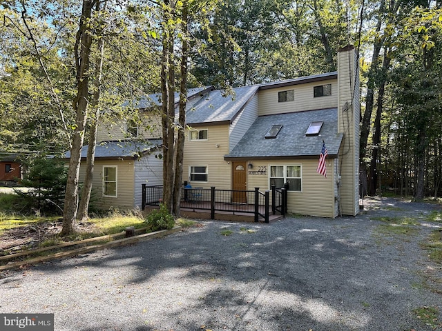 view of front facade featuring a chimney, roof with shingles, and a wooden deck