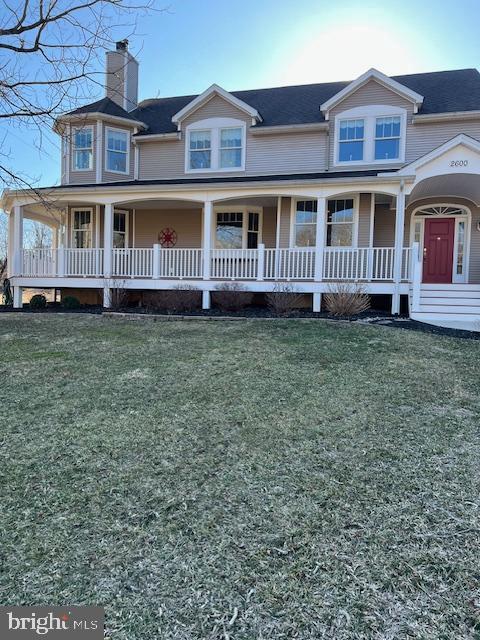 farmhouse inspired home featuring a porch, a front lawn, and a chimney