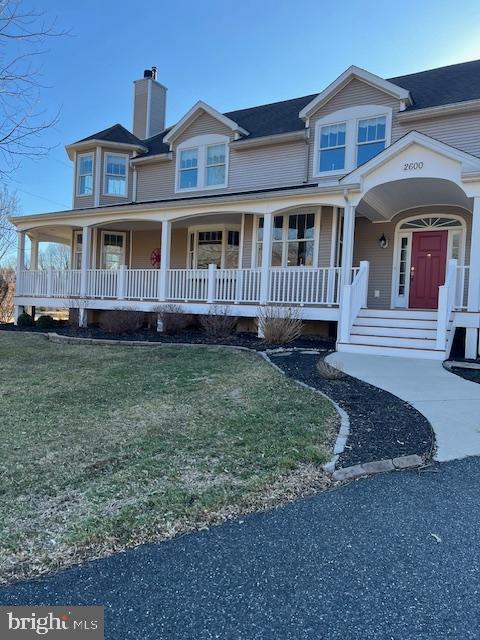 view of front facade featuring a porch, a front yard, and a chimney