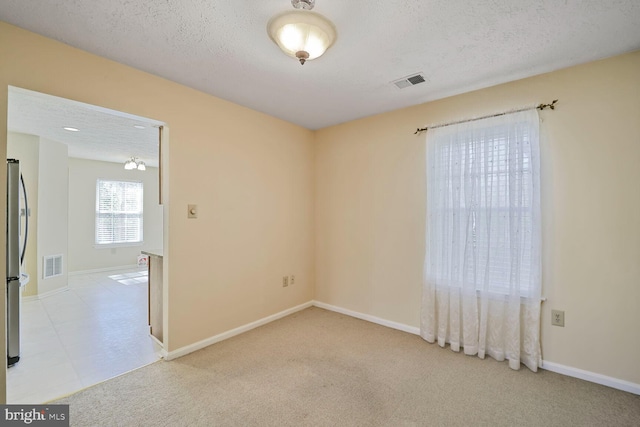 unfurnished room with a textured ceiling, visible vents, and light carpet