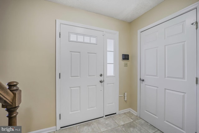 foyer with light tile patterned flooring, baseboards, and a textured ceiling