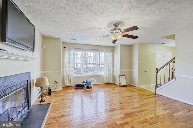 exercise room featuring visible vents, a ceiling fan, a textured ceiling, a glass covered fireplace, and light wood-style floors