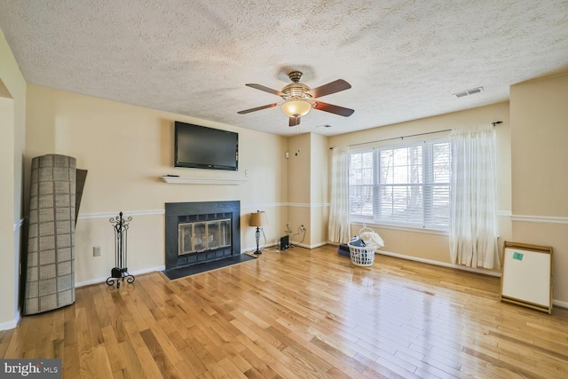 unfurnished living room featuring visible vents, a fireplace with flush hearth, wood finished floors, baseboards, and ceiling fan