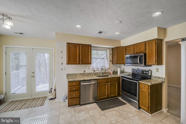 kitchen with light stone countertops, brown cabinetry, a sink, stainless steel appliances, and french doors