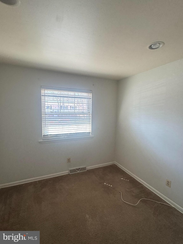 empty room with baseboards, visible vents, and dark carpet