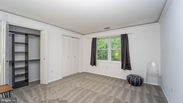 unfurnished bedroom with visible vents, multiple closets, carpet, crown molding, and baseboards