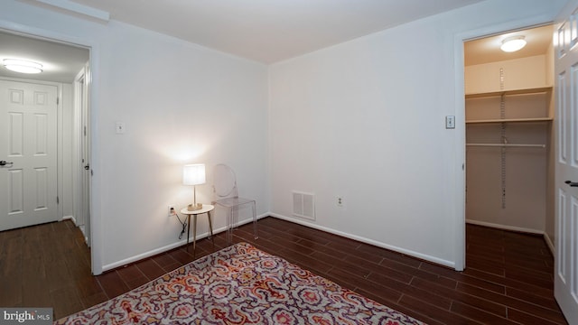 unfurnished bedroom featuring a walk in closet, visible vents, baseboards, and wood finish floors