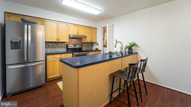 kitchen with a sink, stainless steel appliances, under cabinet range hood, dark countertops, and backsplash