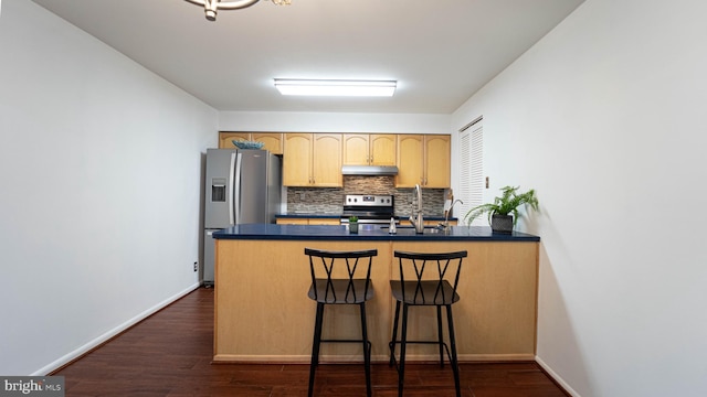 kitchen featuring dark countertops, under cabinet range hood, decorative backsplash, appliances with stainless steel finishes, and a peninsula