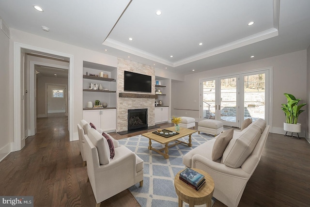 living area with a tray ceiling, plenty of natural light, wood finished floors, and built in shelves