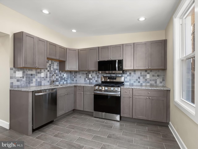 kitchen featuring light stone counters, decorative backsplash, appliances with stainless steel finishes, and a sink