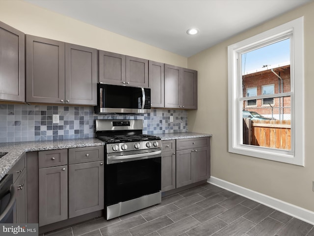 kitchen featuring light stone countertops, baseboards, gray cabinets, stainless steel appliances, and backsplash