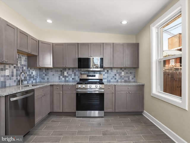 kitchen with a sink, light stone counters, backsplash, appliances with stainless steel finishes, and baseboards