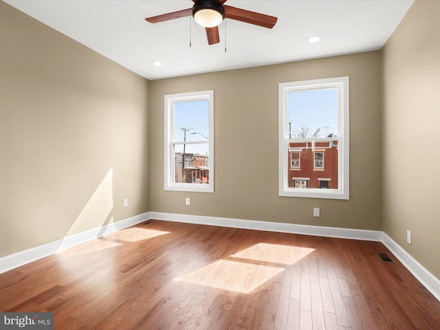 unfurnished room with visible vents, a healthy amount of sunlight, baseboards, and hardwood / wood-style flooring