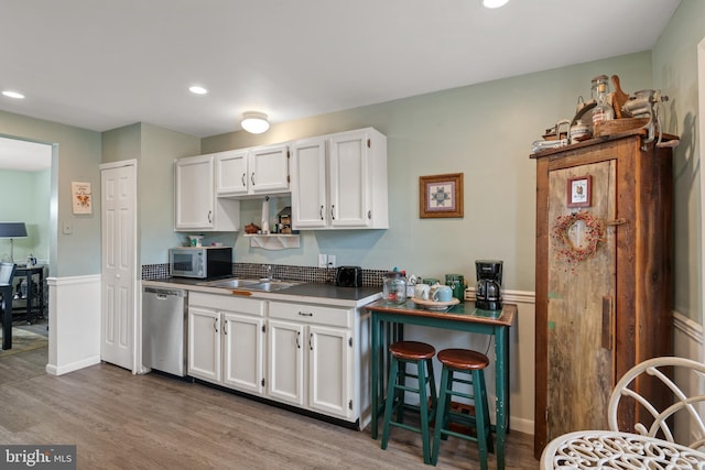 kitchen featuring wood finished floors, recessed lighting, a sink, stainless steel appliances, and white cabinetry