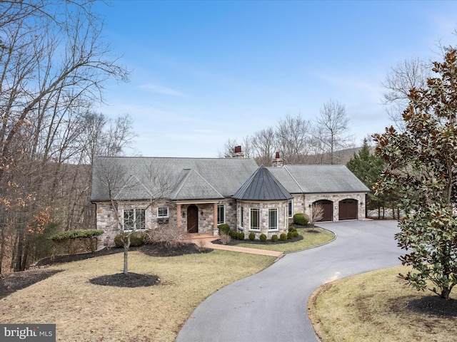 view of front of house featuring stone siding, a chimney, aphalt driveway, and a front lawn