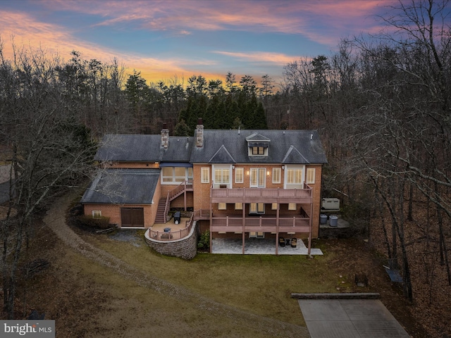 back of house at dusk with a patio, stairway, a wooden deck, a chimney, and a lawn