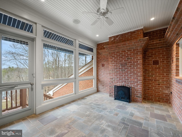 unfurnished sunroom featuring ceiling fan, a brick fireplace, and wooden ceiling