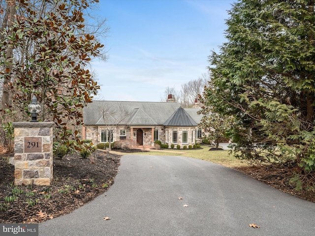 view of front of house featuring a standing seam roof, stone siding, driveway, and metal roof