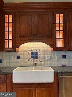 kitchen featuring glass insert cabinets, tasteful backsplash, stainless steel dishwasher, and brown cabinetry