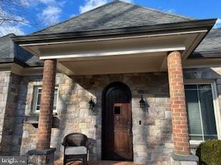 entrance to property with stone siding and a shingled roof