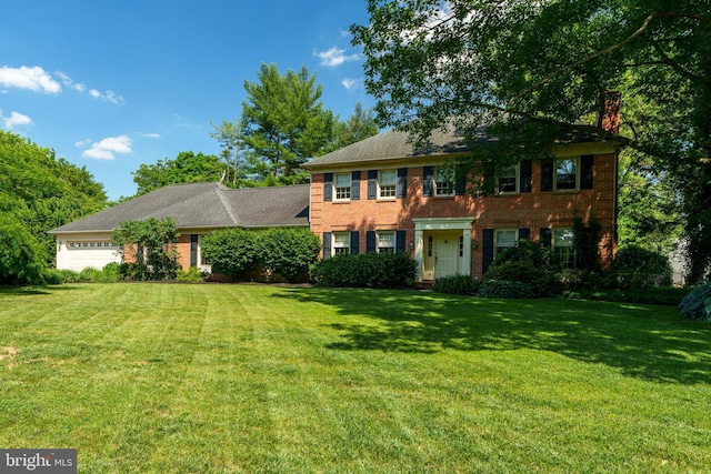 colonial inspired home with brick siding, a garage, a chimney, and a front lawn