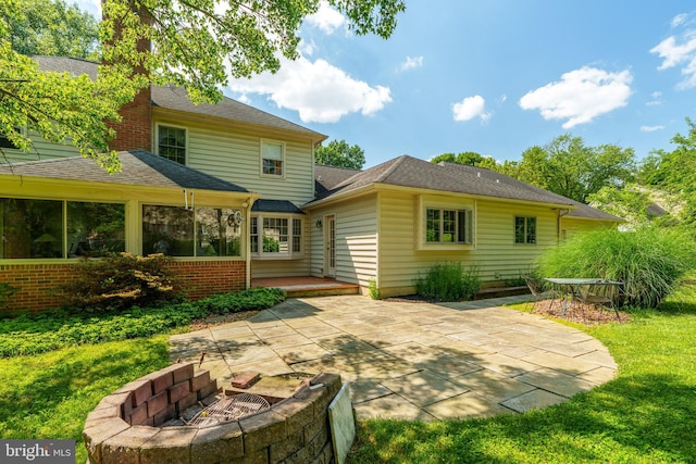 rear view of house with brick siding, roof with shingles, an outdoor fire pit, and a patio area