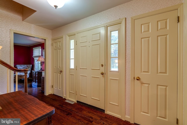 foyer entrance with wallpapered walls, stairs, and dark wood-style flooring