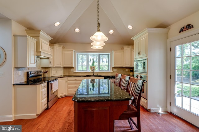 kitchen with a sink, stainless steel appliances, light wood-style floors, and vaulted ceiling