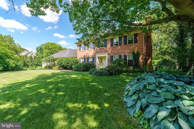 colonial-style house with brick siding, a chimney, and a front yard