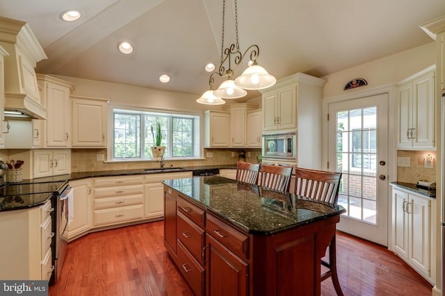 kitchen featuring wood finished floors, a breakfast bar, a sink, appliances with stainless steel finishes, and tasteful backsplash