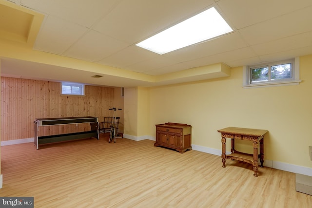 basement featuring light wood finished floors, a drop ceiling, and baseboards