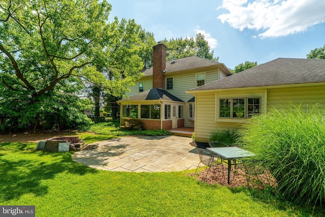 back of property featuring a yard, a chimney, a patio, and roof with shingles