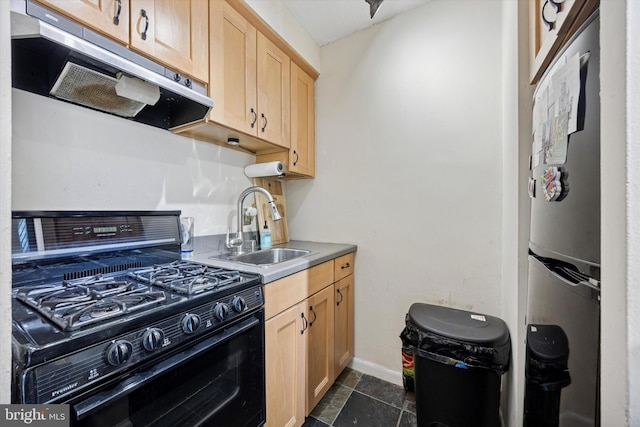 kitchen with light brown cabinetry, black gas range, under cabinet range hood, a sink, and freestanding refrigerator