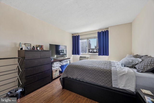 bedroom with a wall unit AC, wood finished floors, and a textured ceiling