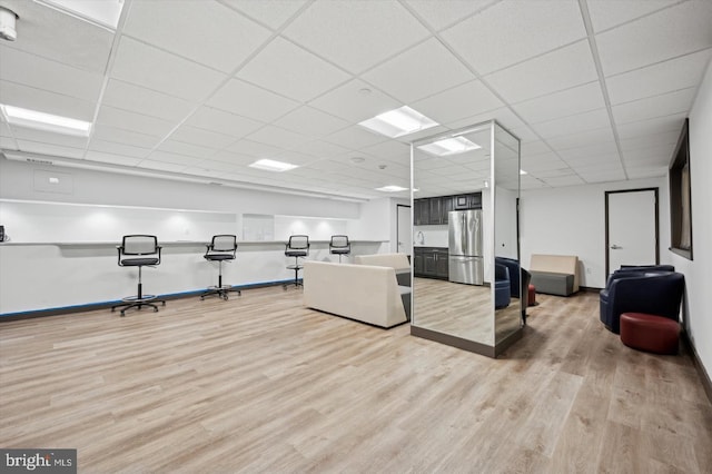 workout room featuring baseboards, light wood-type flooring, and a paneled ceiling