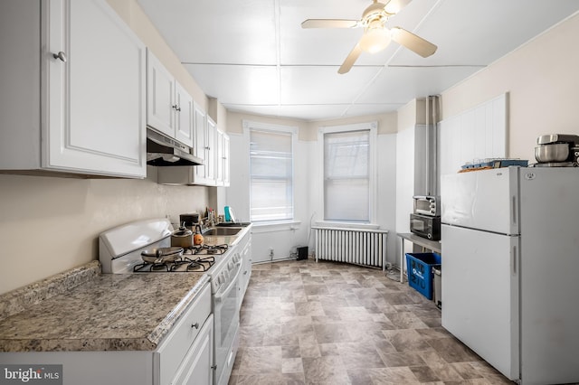 kitchen featuring white appliances, radiator, under cabinet range hood, stone finish flooring, and white cabinetry