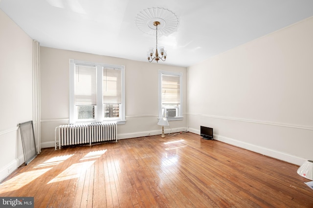 unfurnished room featuring baseboards, radiator, a chandelier, and hardwood / wood-style flooring