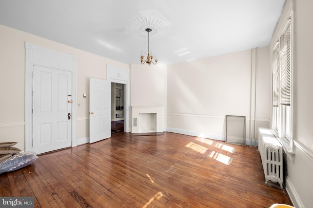 unfurnished living room with hardwood / wood-style floors, radiator heating unit, baseboards, and a chandelier