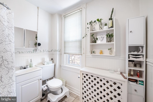 bathroom featuring vanity, toilet, a wainscoted wall, and tile patterned flooring