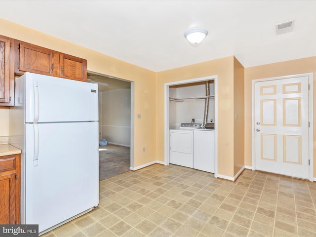 kitchen with visible vents, brown cabinets, independent washer and dryer, freestanding refrigerator, and light countertops