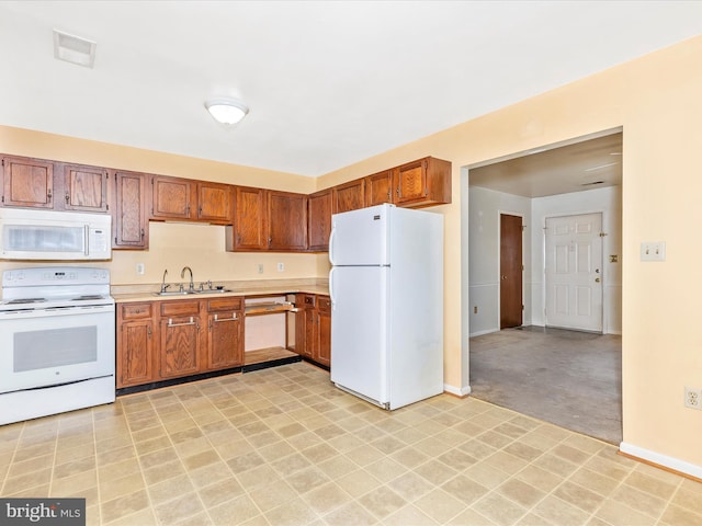 kitchen with white appliances, brown cabinetry, light countertops, and a sink