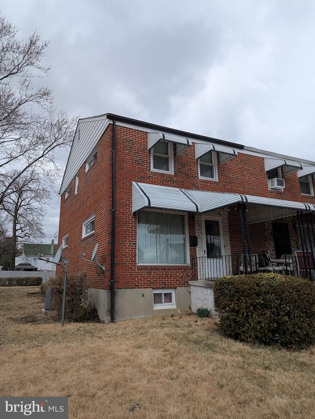 view of front of property featuring brick siding, covered porch, a front lawn, and a wall unit AC