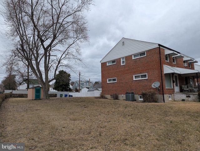 view of side of property featuring central air condition unit, a lawn, fence, an outdoor structure, and brick siding