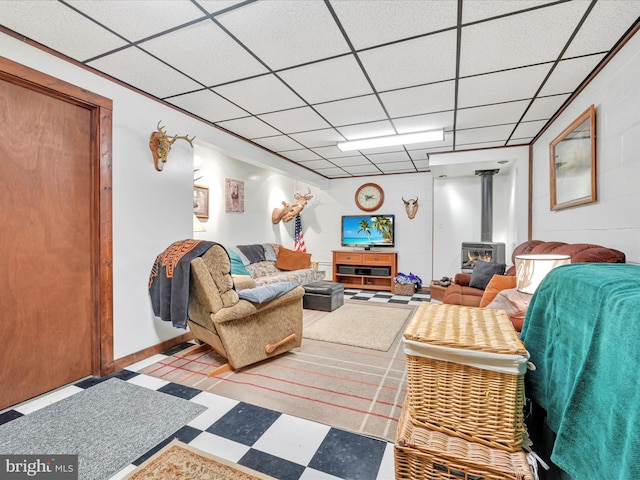 living room with tile patterned floors, concrete block wall, a wood stove, and a paneled ceiling